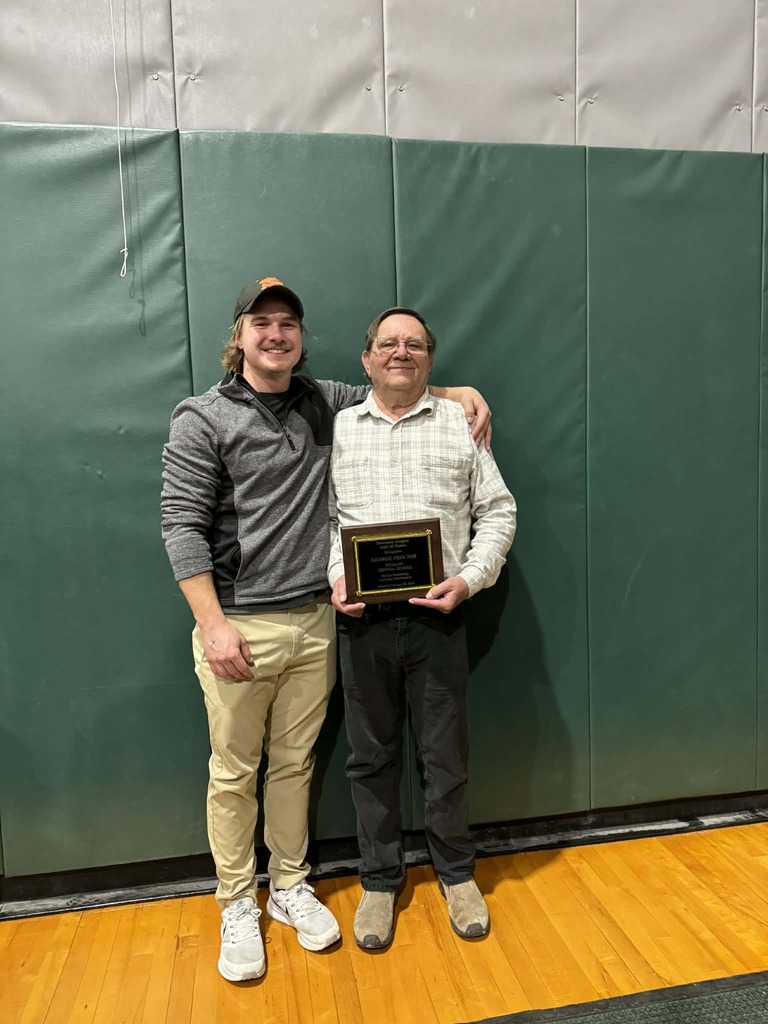 George Proctor stands in front of a green back ground holding his award.