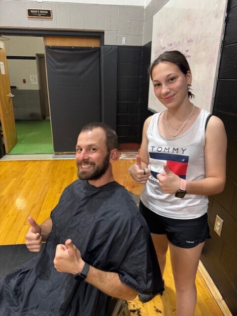 Anthony Camillone sits in a cair with a barber shop cover on and his thumbs up, Gabby Miraglio stands behind him with her thumbs up after recently giving him a haircut.