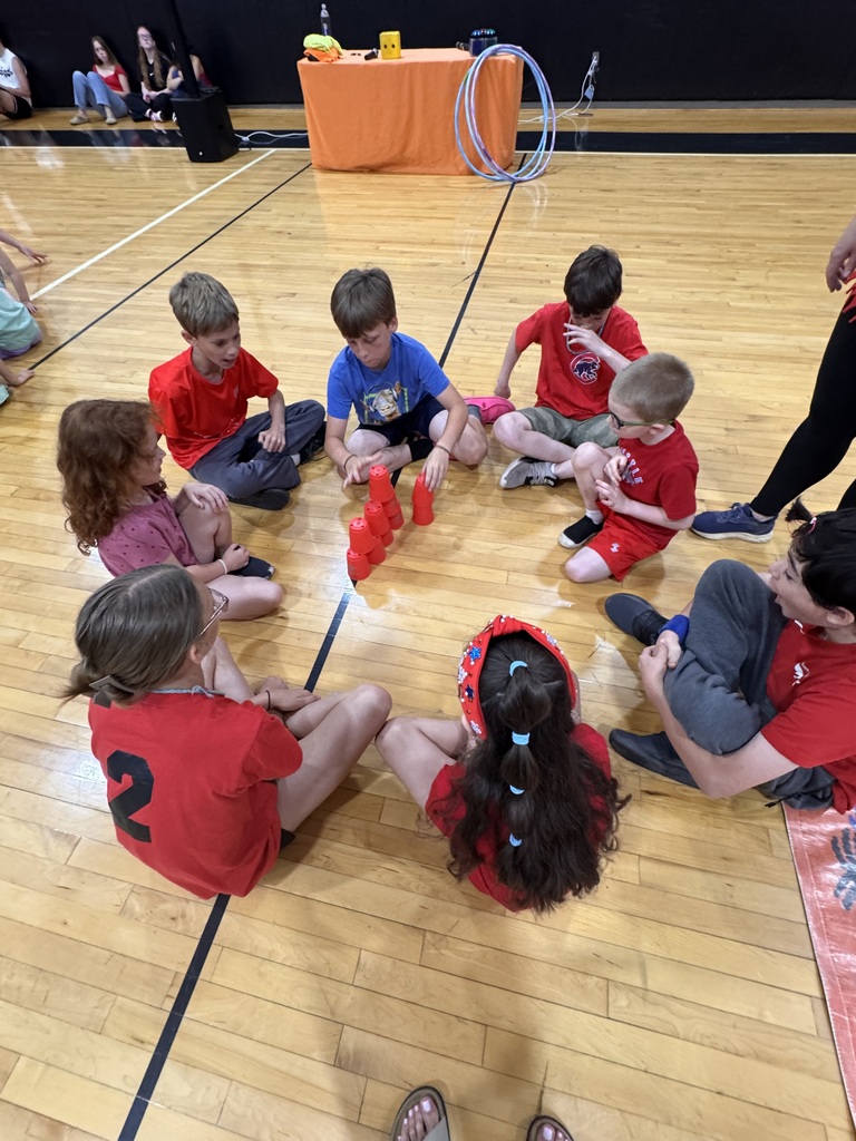 red team members circle around a stack of cups to work together for a board game event