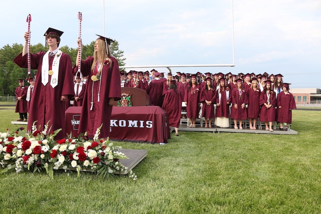 Graduation Marshals Sam Parker and Faith Mabee stand with batons raised in front of graduates on the risers. 