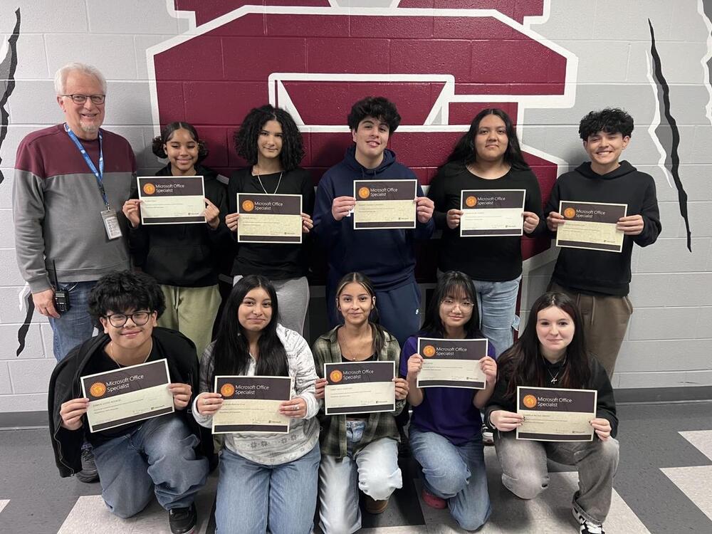Students hold certificates of achievement as teacher stands by