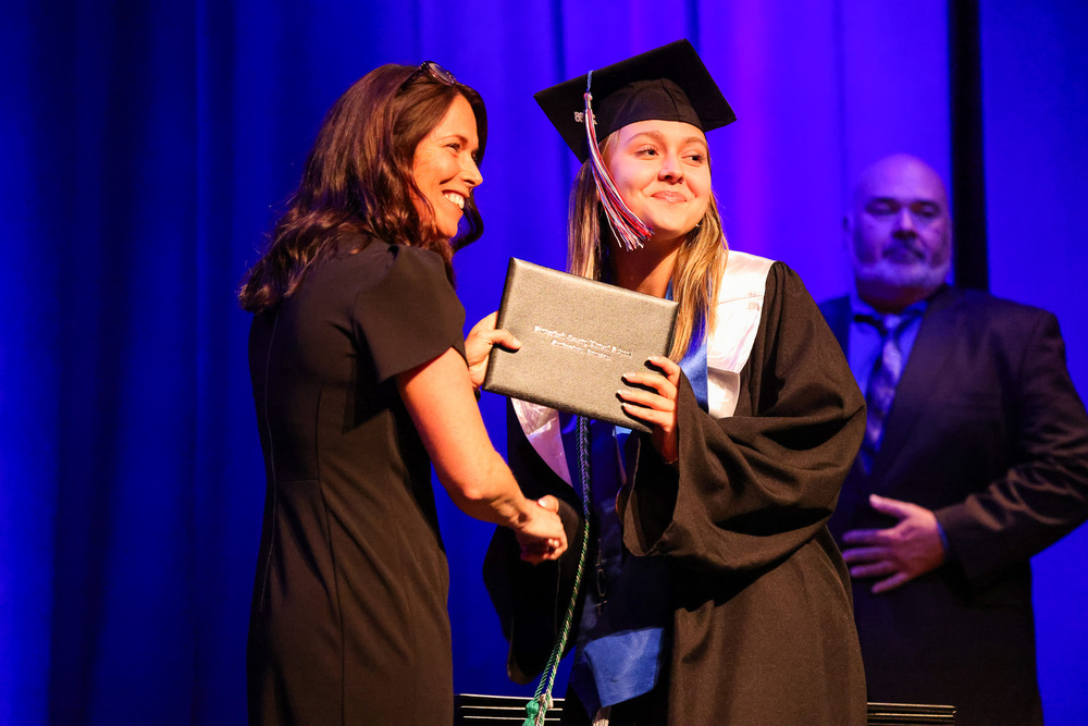 Principal hands diploma to student in cap and gown