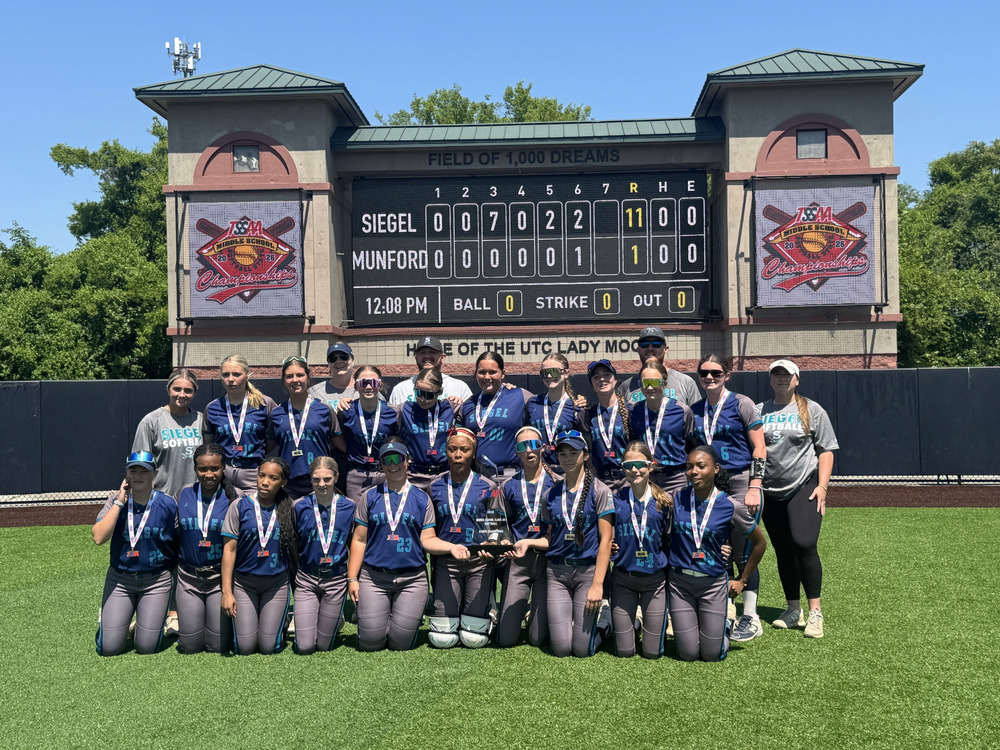 Softball team with championship trophy in front of scoreboard