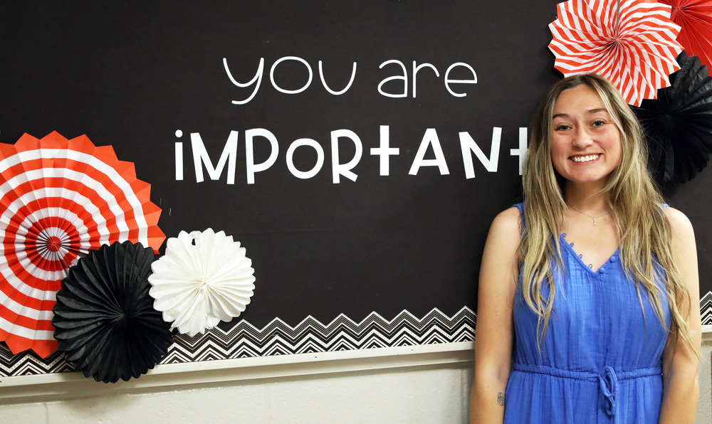 Woman in blie dress smiles in front of bulletin board saying "you are important"