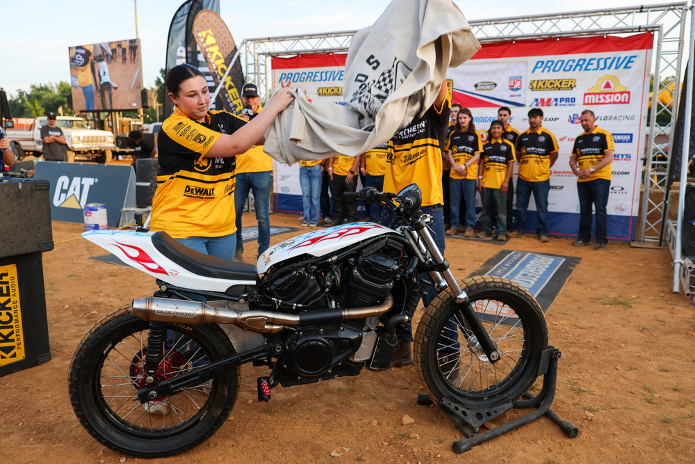 Female student in black and yellow shirt takes cover off motorcycle