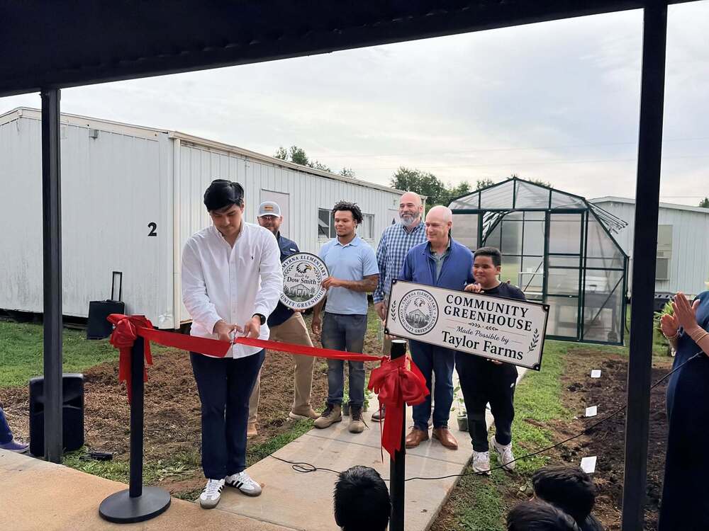 Man in white shirt cuts ribbon on green house