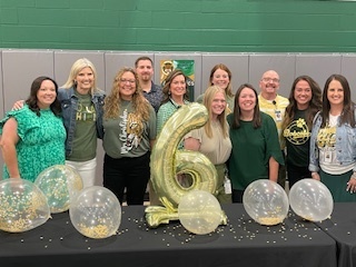 Group of adults posing behind a table with balloons and a large number 6 in the center.