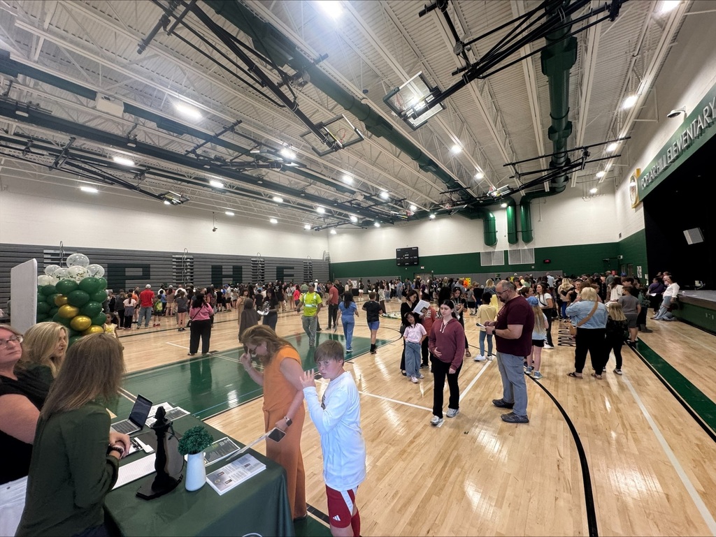 A large indoor basketball court with a crowd of people, some standing, some sitting at a table, and others walking.