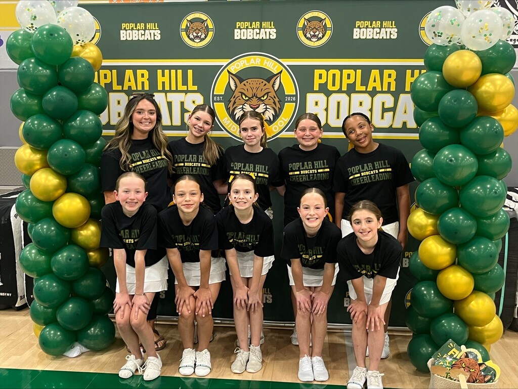 A girls' basketball team in black shirts and white shorts poses in front of a green and yellow balloon arch.