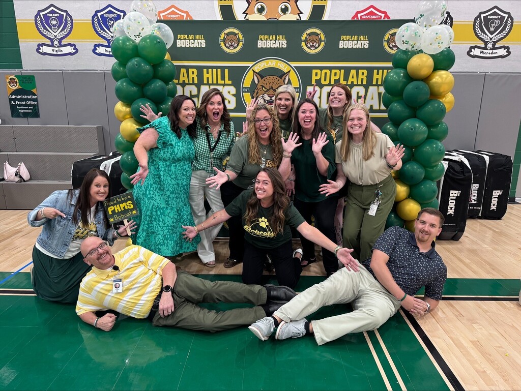 A group of people pose for a picture in a gym with balloons in the background.