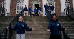 Several students in matching blue jackets and pants on a concrete staircase in front of a brick building.