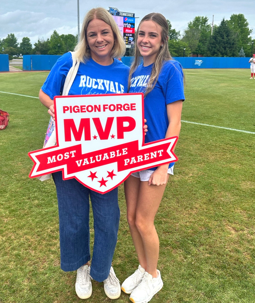 Two women smiling for picture in front of Softball field, holding sign that reads, "Pigeon Forge, M.V.P, Most Valuable Parent."