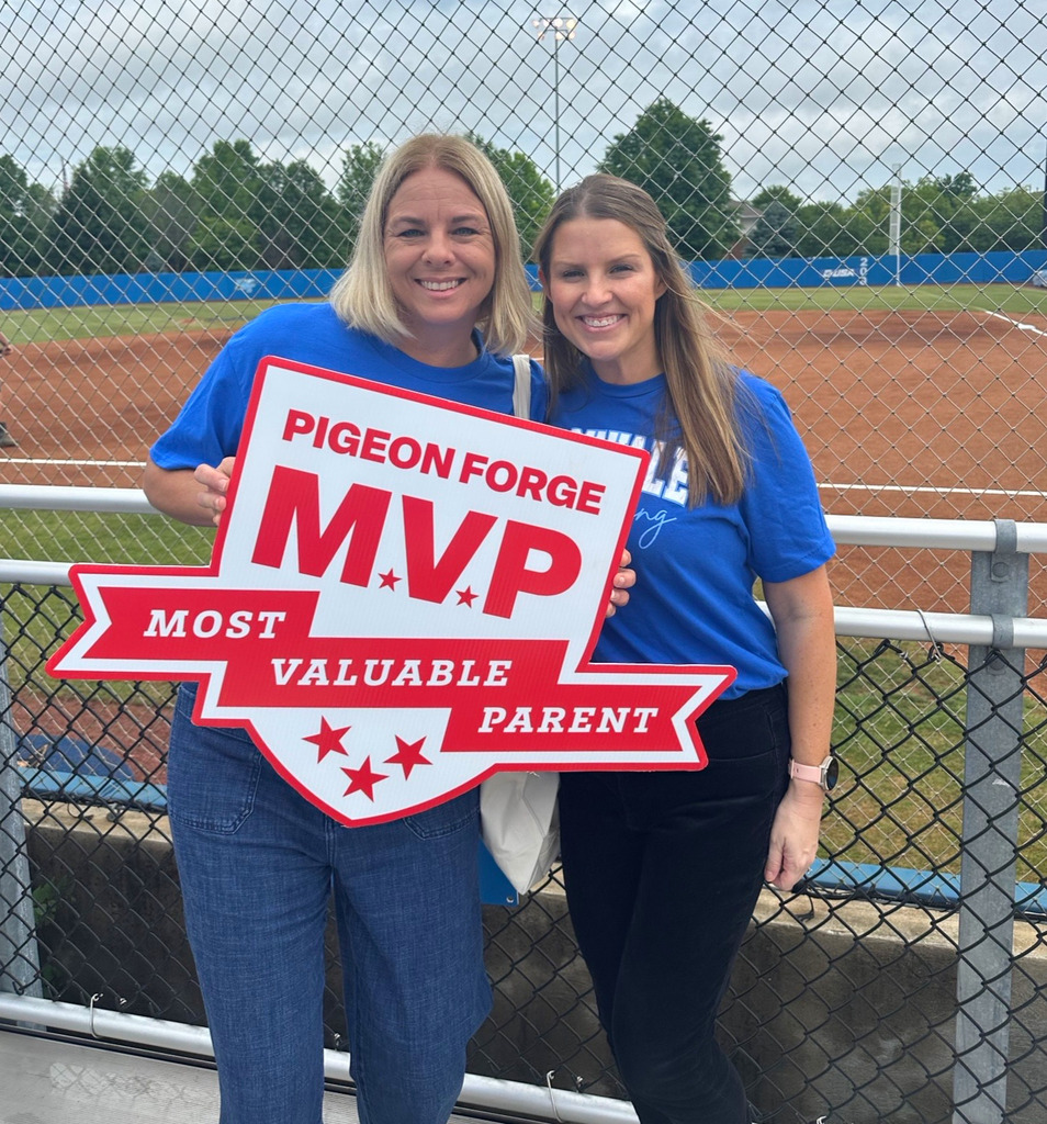 Two women smiling for picture in front of Softball field, holding sign that reads, "Pigeon Forge, M.V.P, Most Valuable Parent."