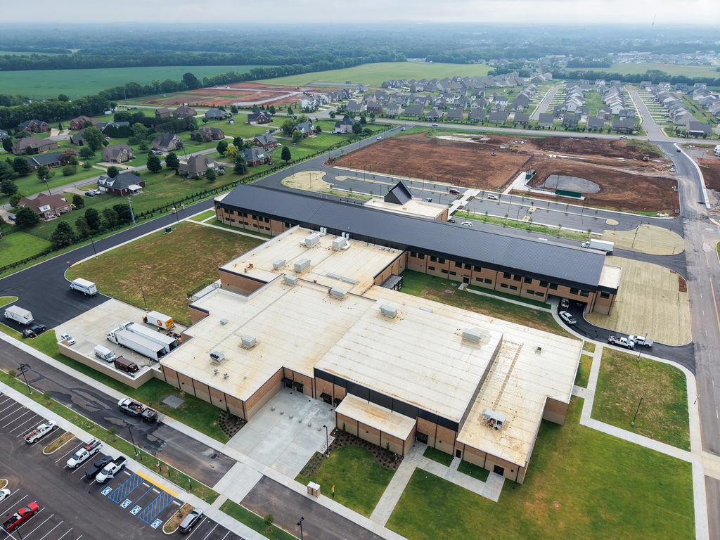 Aerial view of a large building with flat roofs, a parking lot, and a landscaped area.