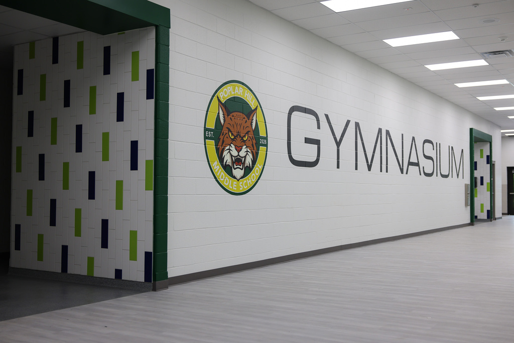 Empty hallway with a logo featuring a cat, "GYMNASIUM" written above, white walls, and an open door.