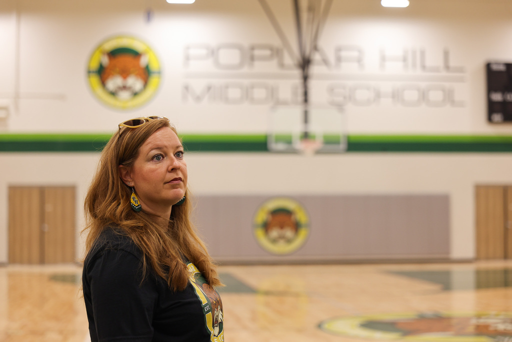 A woman stands in a basketball court with a wall behind her. The wall reads "Popular Hill Middle School."