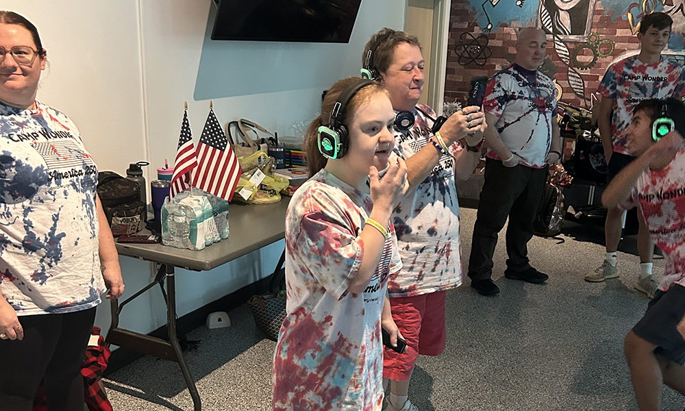 Adults and children in tie-dye shirts, some with headphones, standing in a room with a table.