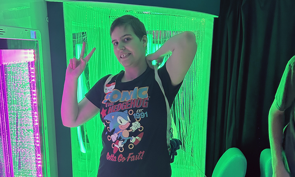 A person in a black Sonic the Hedgehog t-shirt, making a peace sign in front of a green light.