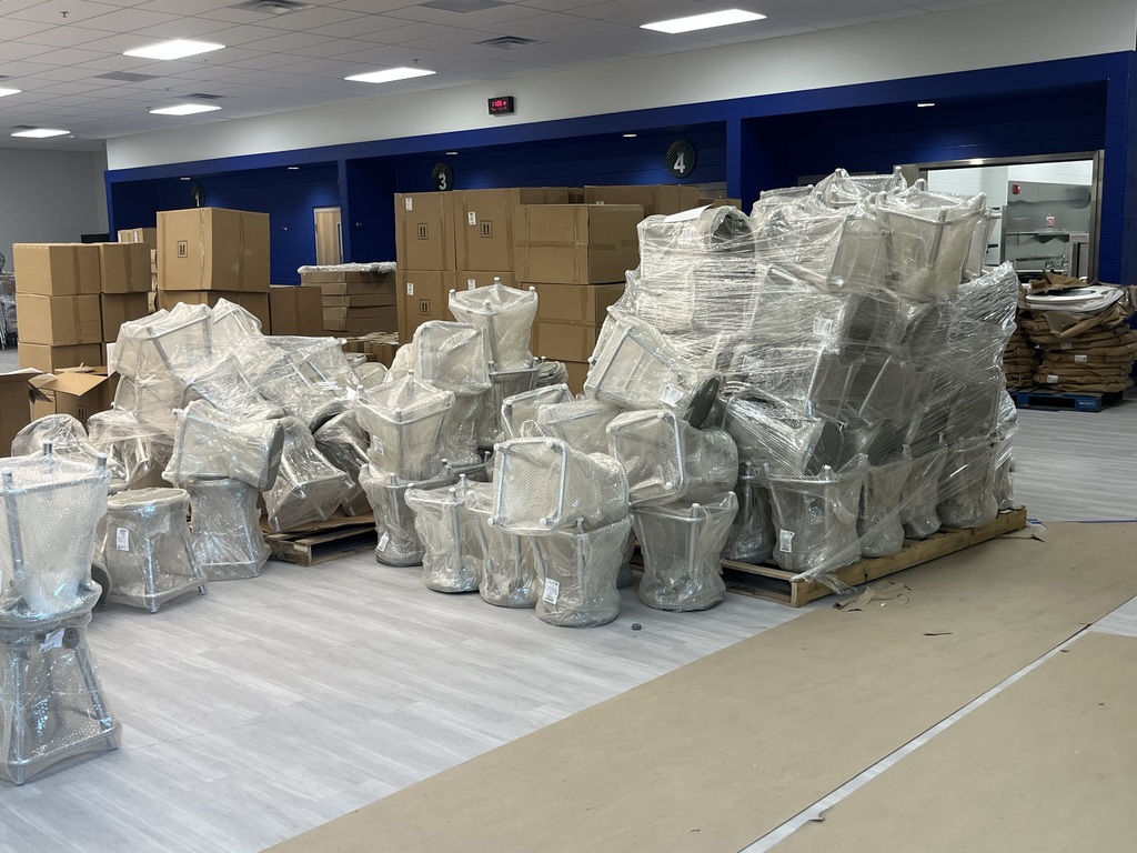 An indoor space with multiple boxes and furniture wrapped in plastic on a floor. Some boxes are stacked.