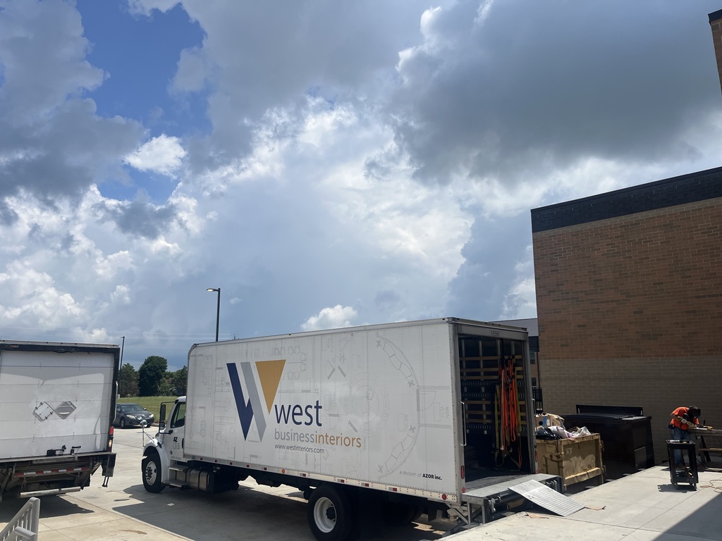 A white moving truck with "West" written on it parked next to a building, with boxes and a ramp.