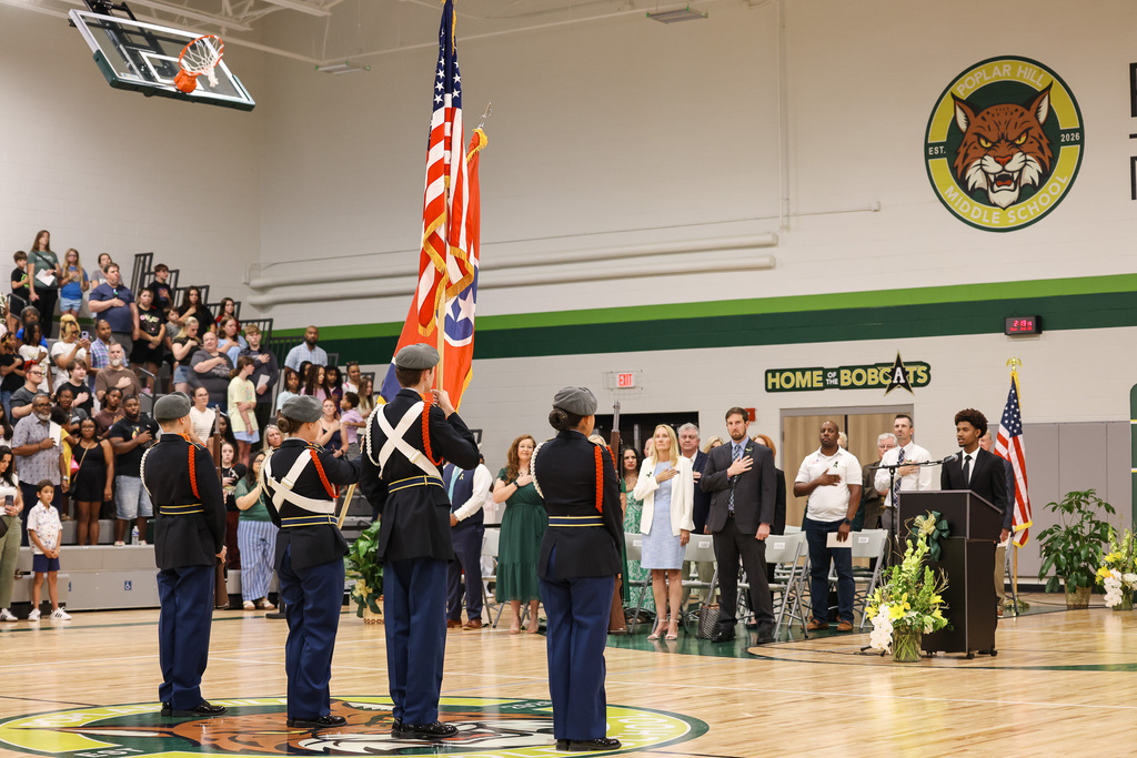 Ceremony on a basketball court with military personnel, flags, and spectators in the stands.