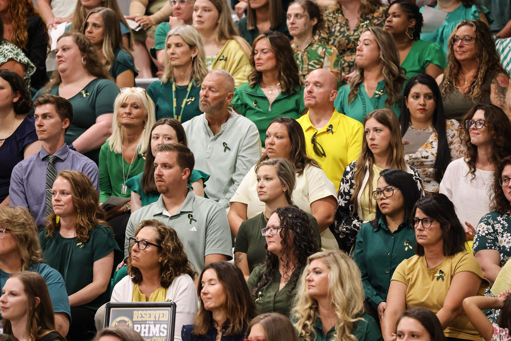 Many people in a stadium, wearing green and yellow shirts, watching an event, some wearing glasses.