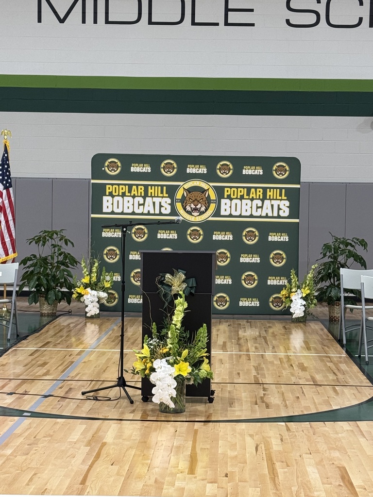 A basketball court with a podium, flowers, and banners with the text "Poplar Hill Bobcats". A flag stands at the left side.