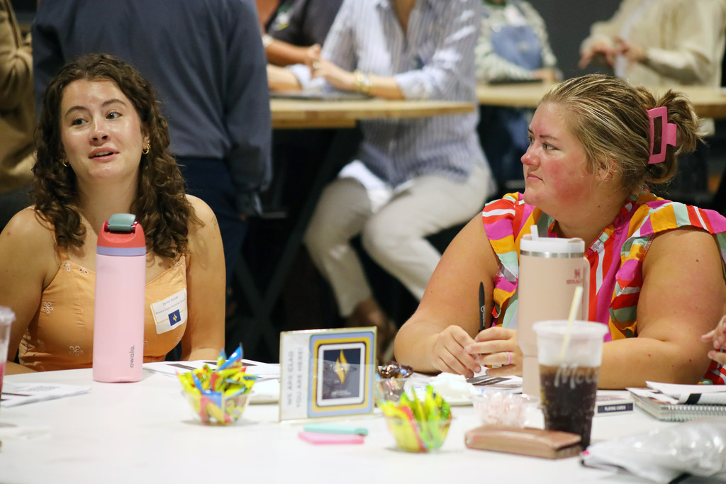 Two women sit at a table, one wearing a colorful type.