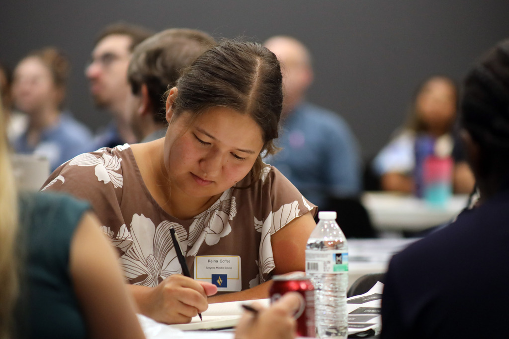 A woman wearing a brown top writes in a notebook.