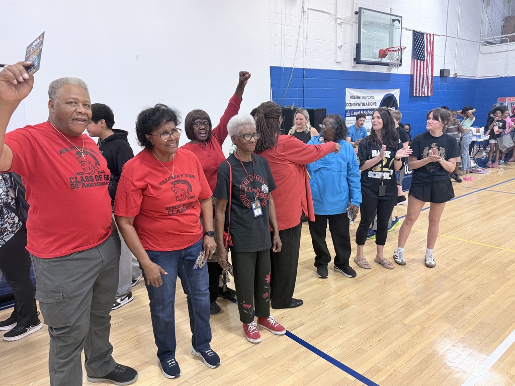 Group of adults wearing red and black shirts, standing on a basketball court with a blue wall in the background.