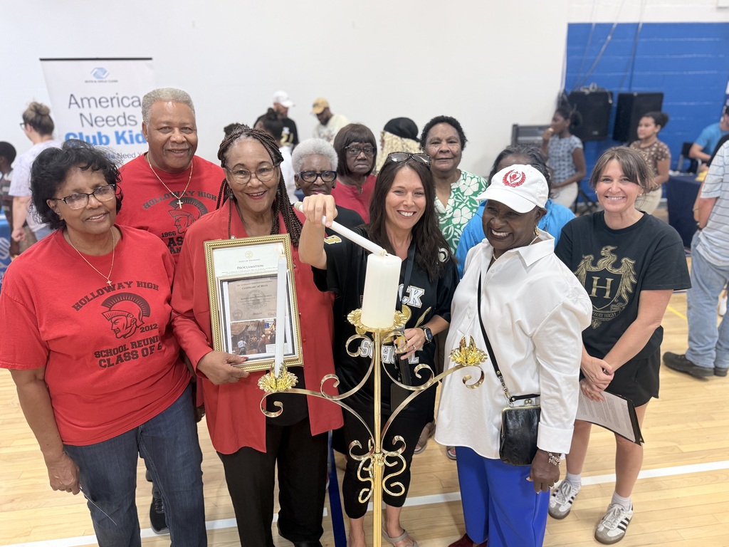 Nine people pose for a photo in a gym; one person holds a lit candle in a candleholder.
