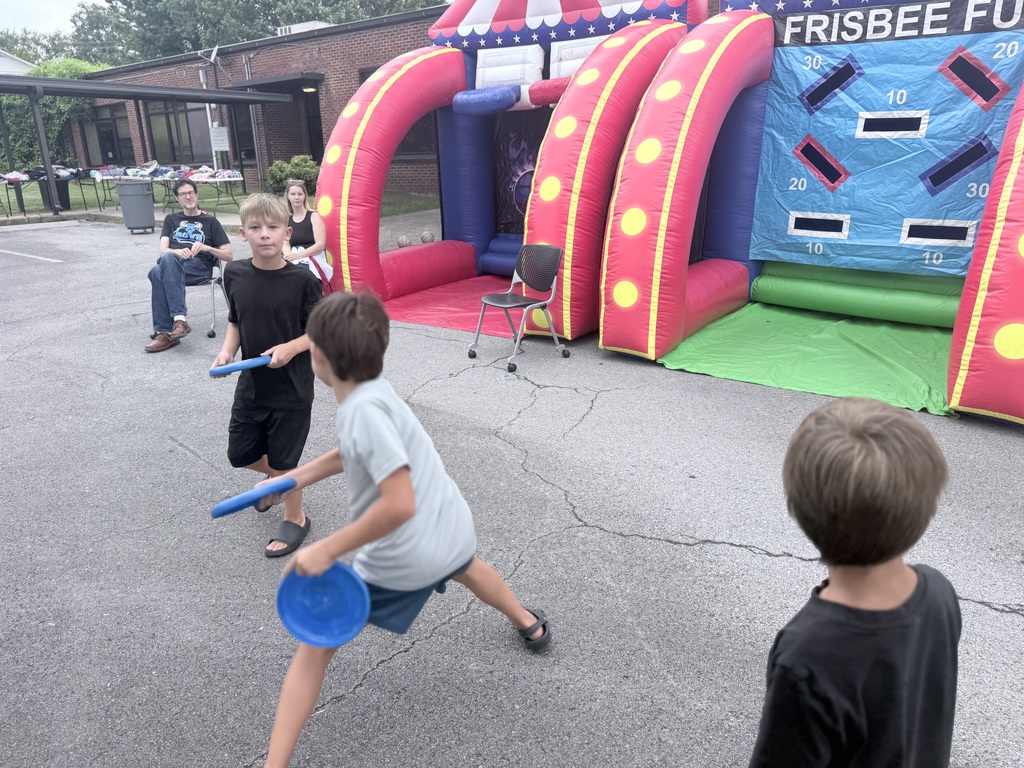 Kids play frisbee in front of a large inflatable obstacle course with a red, yellow, and green color scheme.