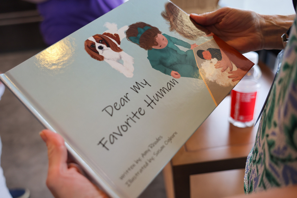 A person holding a book titled "Dear My Favorite Human" with an illustration of a dog and person.