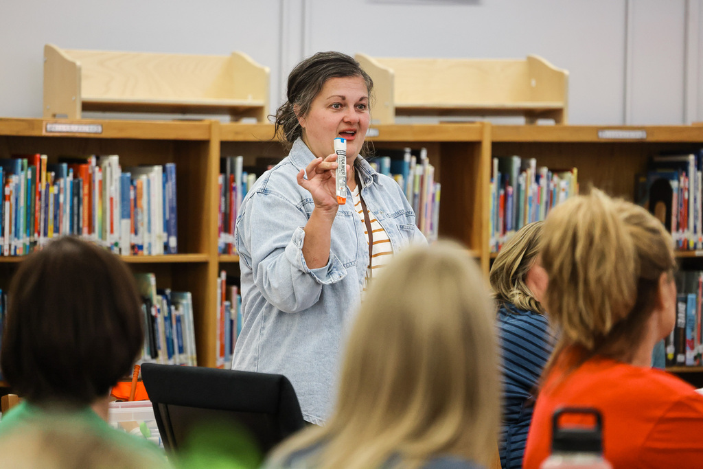 Woman standing in a library, holding a toothbrush, with several women seated before her.