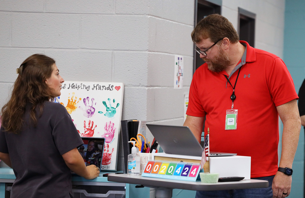 A man and woman stand at a table with a laptop, colored cubes, and other items.
