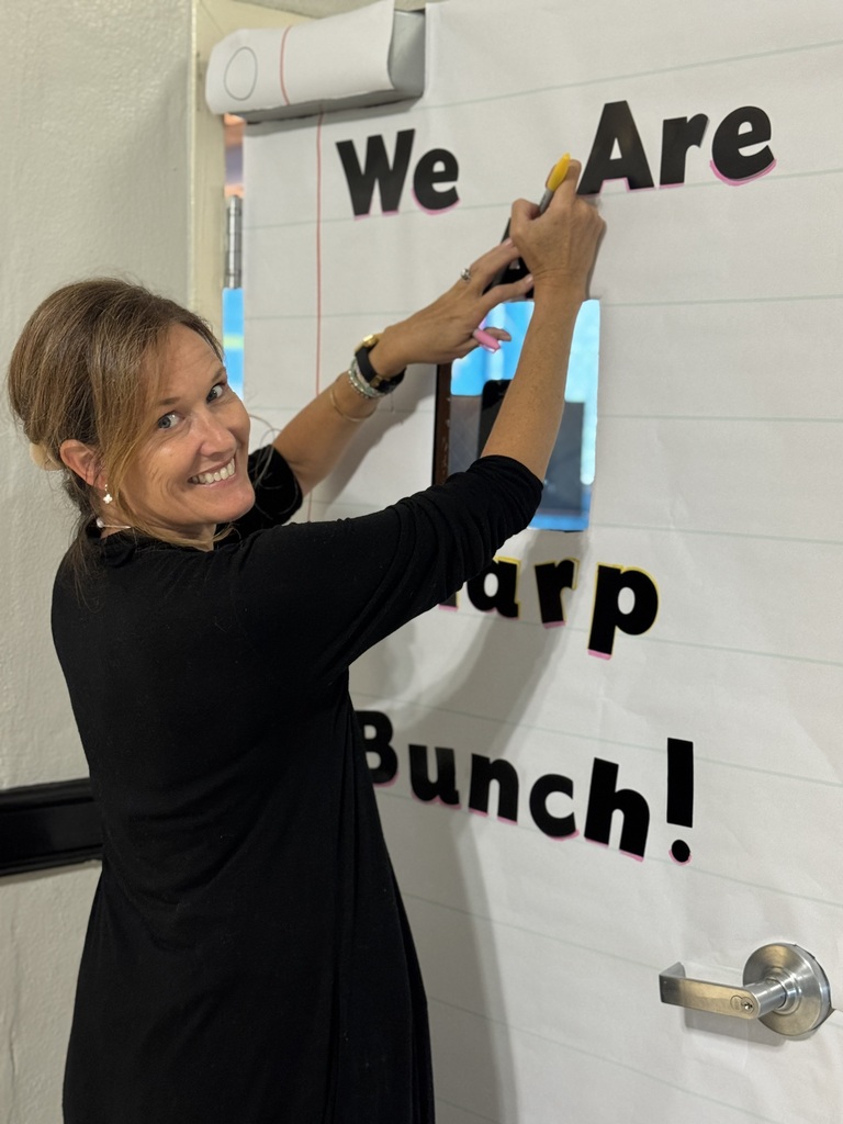 A woman wearing a black dress is using a marker to write on a bulletin board that says "We Are Sharp Bunch!"