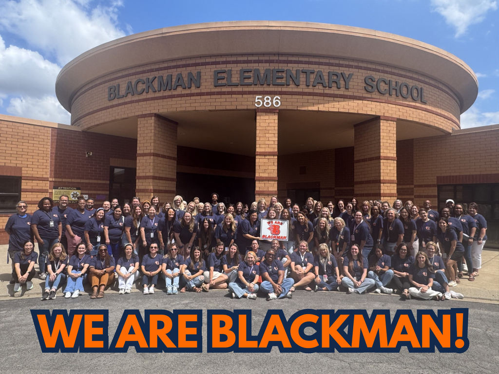 A large group of people in blue shirts pose in front of Blackman Elementary School.