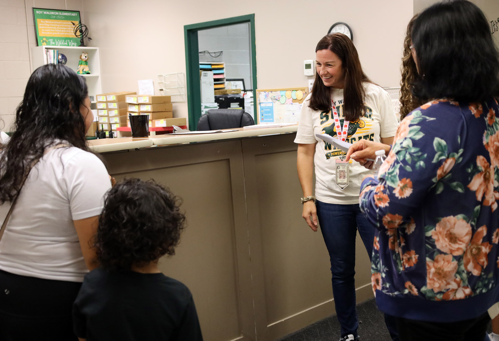 A group of people, including a woman in a floral top, converse in a room with a beige counter.