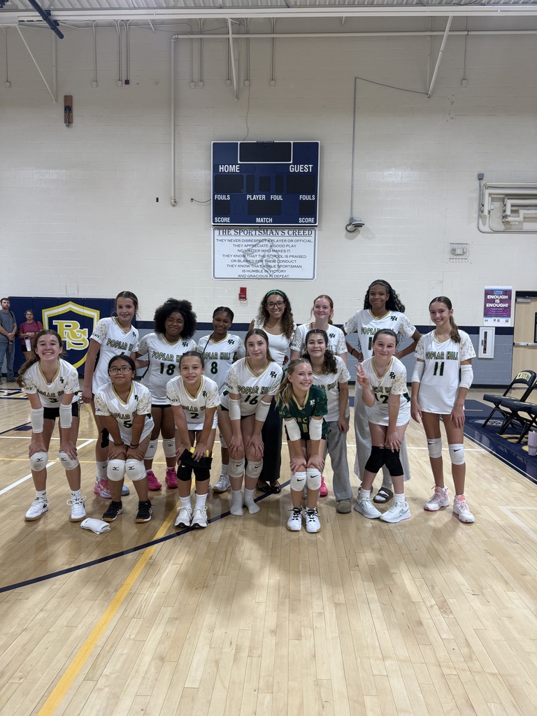 A group of women in white uniforms stands on a gym floor, smiling and posing for a team photo.