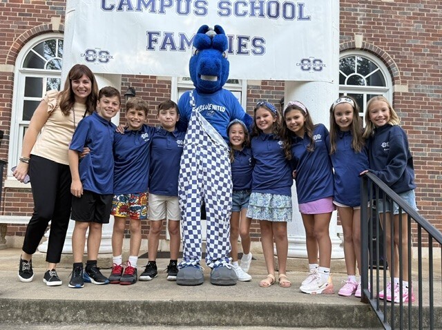 Group of students, teachers, and a mascot pose in front of a brick building with Campus School Families banner.