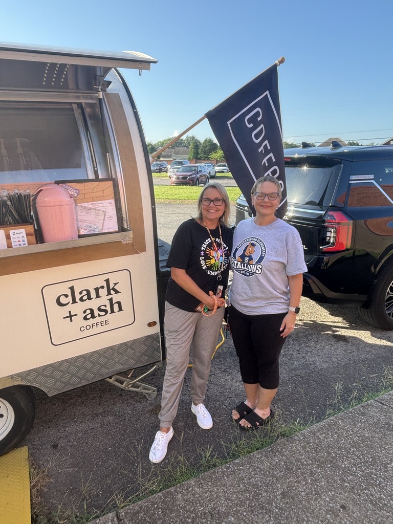 Two women stand next to a coffee trailer with a banner that reads "COFFEE" and "clark + ash" in white letters.