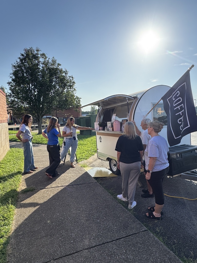 People gather near a food truck with a banner reading "COFFEE" on a sunny day.