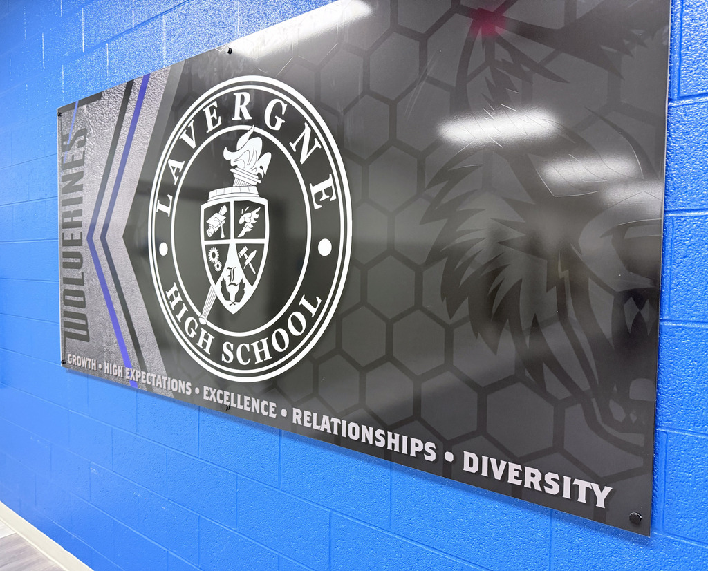 A wall displays a reflective sign with a school logo. The background is blue with hexagons and a wolf.