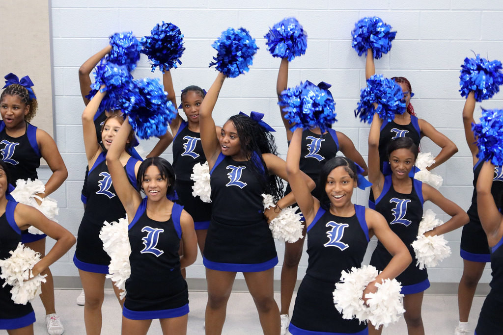 A cheerleading squad with blue and white pom-poms, all dressed in matching black and blue uniforms.