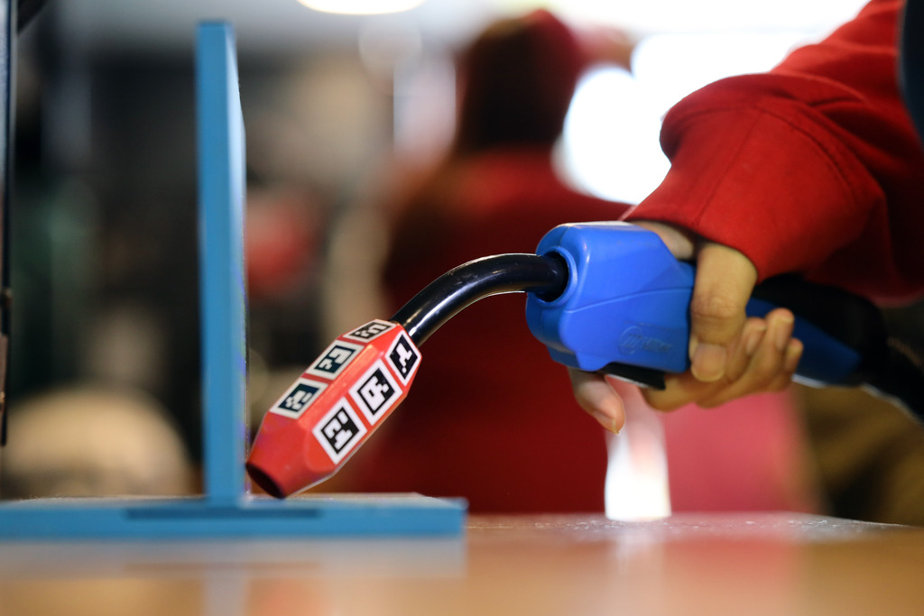 A person holds a red and blue welding simulator with symbols and numbers over a blue stand.