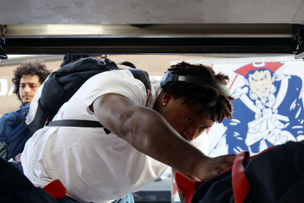 Football player loads travel bag on to bus with oakland patriots logo in background