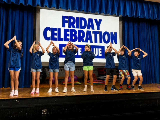 A group of children performing on a stage with a banner saying "FRIDAY CELEBRATION."