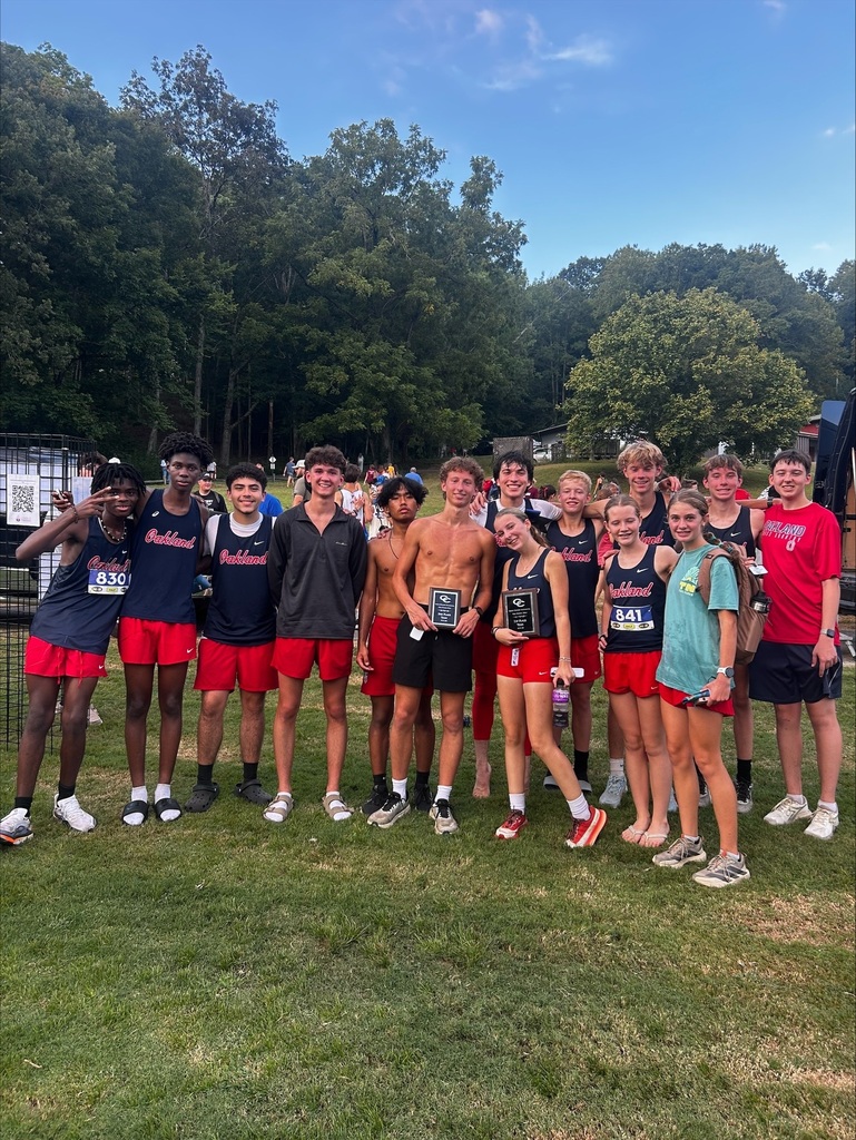 Group of people wearing running gear and holding awards, standing on a grassy field. Trees in the background.