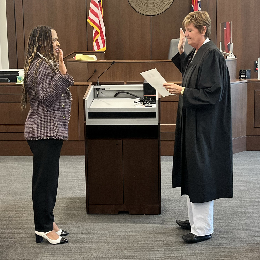 A woman in a black robe and white pants speaks to another woman in a purple coat.