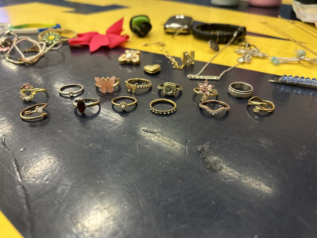 A table displays various jewelry pieces, including rings, necklaces, and bracelets, on a black surface with a yellow border.